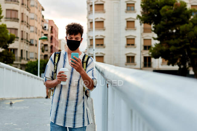 Jovem afro homem com máscara está andando enquanto ele está usando seu telefone — Fotografia de Stock
