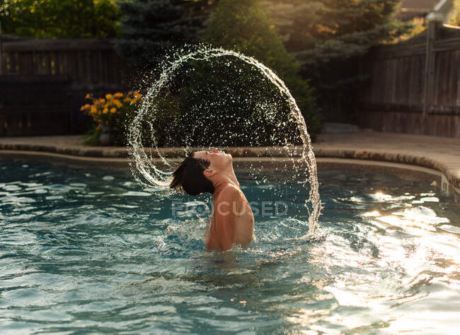 Teenage boy flipping water from his hair in an arc in a backyard pool. — Stock Photo