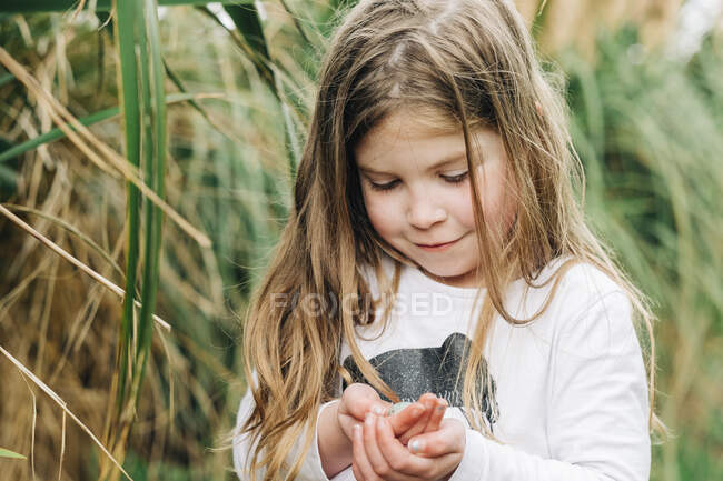 Jovencita sosteniendo un pequeño huevo de pájaros en sus manos - foto de stock