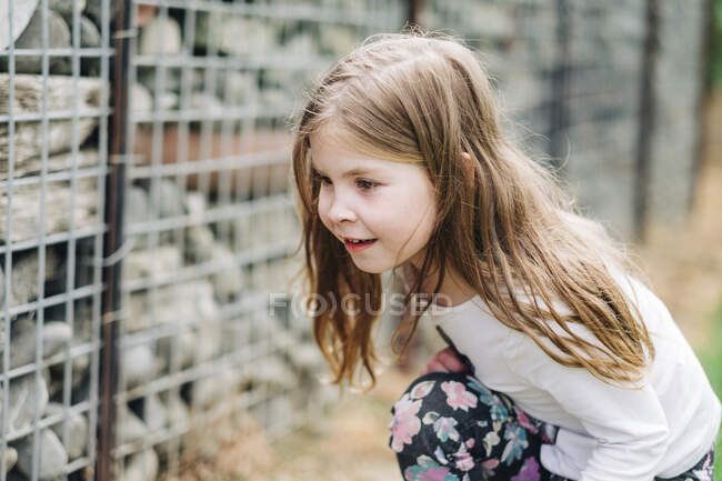 Menina jovem agachado para baixo e à procura de insetos em uma parede de rocha — Fotografia de Stock