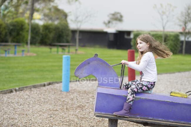 Молодая девушка играет на качающейся лошади на детской площадке — стоковое фото