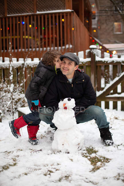 Filho beijando seu pai depois que eles construíram um boneco de neve em seu quintal — Fotografia de Stock