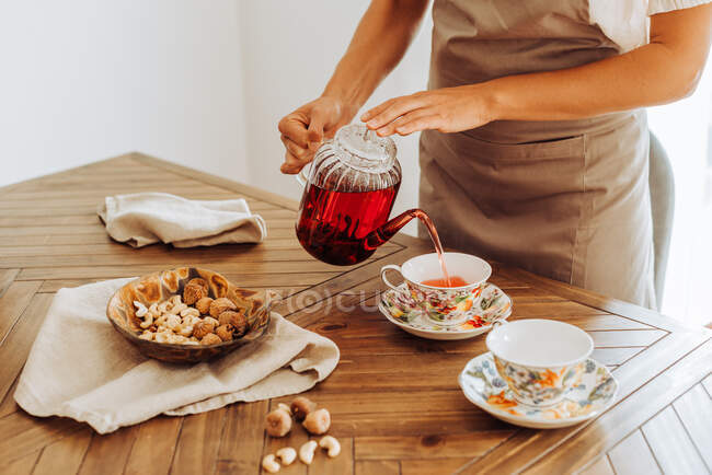 Tiro recortado de mulher com chá na mesa na cozinha acolhedora — Fotografia de Stock
