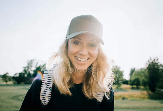 Retrato de una mujer con el pelo alborotado y una gorra sonriendo en verano - foto de stock