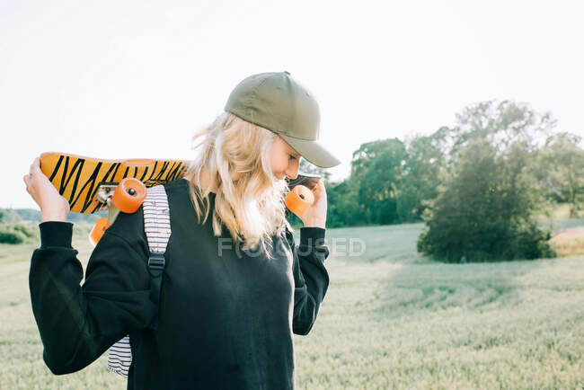 Жінка тримає скейтборд, перебуваючи в сільській місцевості на заході сонця — стокове фото