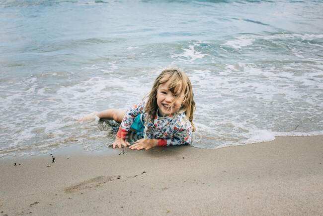 Giovane ragazza sdraiata in acqua in spiaggia sorridente — Foto stock
