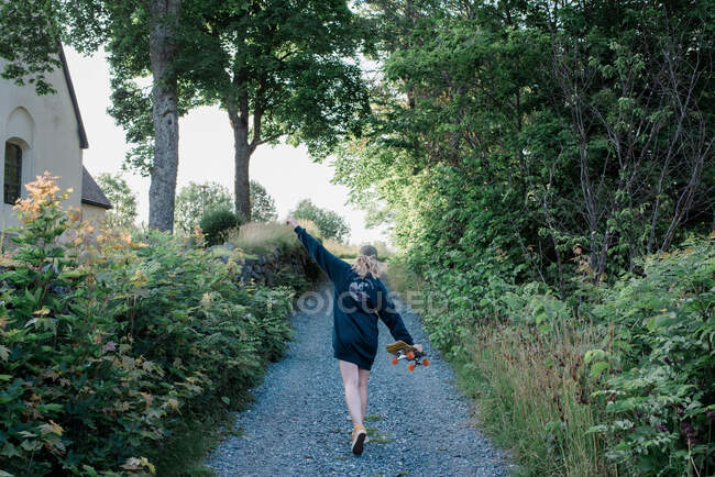 Frau tanzt im Sommer mit ihrem Skateboard in einer Feldstraße — Stockfoto
