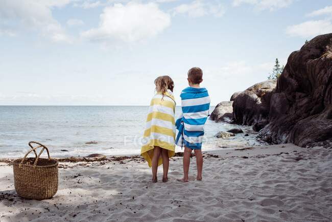 Boy and girl stood on the beach wrapped in towels looking at the ocean — Stock Photo