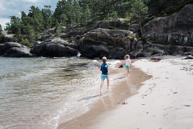 Hermano y hermana corriendo por la arena juntos en la playa - foto de stock