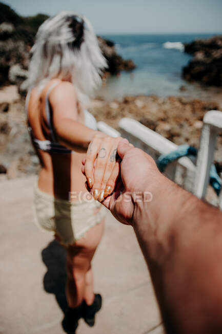Un couple sur la plage marche main dans la main. Perspective du bras de l'homme — Photo de stock