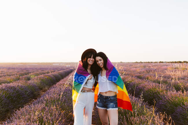 Дівчата на полі лаванди посміхаються блискучим прапором гордості. — стокове фото