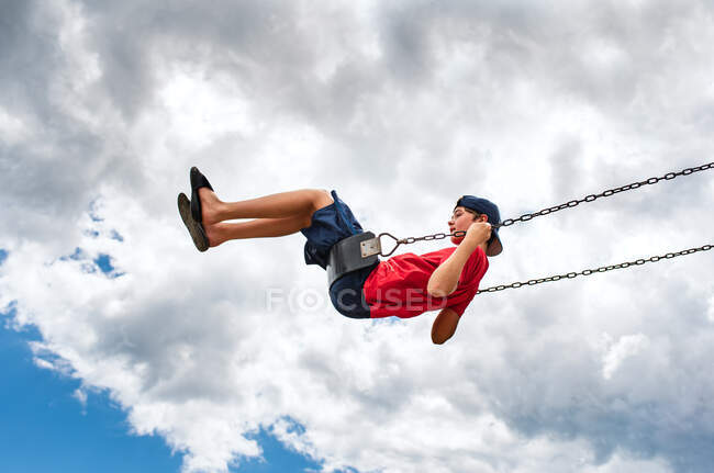 Vista lateral do menino em um balanço com apenas céu nublado no fundo. — Fotografia de Stock