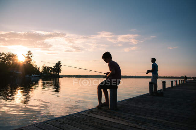 Father and son fishing on a dock of lake at sunset in Ontario, Canada. — Stock Photo