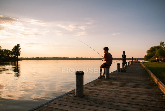 I ragazzi pescano sul molo di un lago al tramonto in Ontario, Canada. — Foto stock