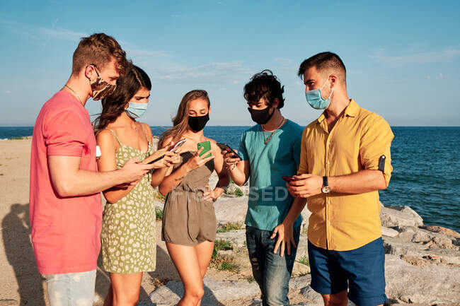 Un gruppo di giovani che indossano maschere e telefoni cellulari in una giornata estiva — Foto stock