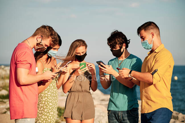Un grupo de jóvenes con mascarilla facial y teléfonos móviles en un día de verano - foto de stock