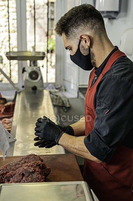 Macellaio con maschera Preparazione di hamburger crudi di manzo in macelleria — Foto stock
