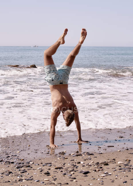 Giovane uomo fa acrobazie con le mani sulla spiaggia — Foto stock