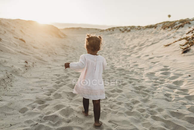 Маленька дівчинка в білій сукні, що йде на пляжі — стокове фото