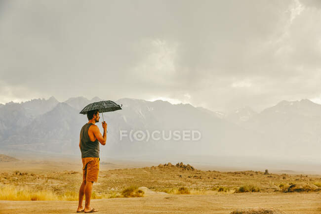 Jeune homme dans le désert de Californie du Nord, tenant parapluie sous la pluie — Photo de stock