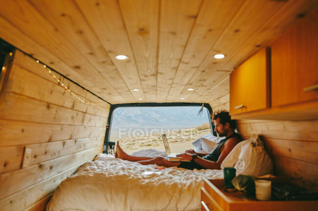 Giovane sul letto con computer portatile in camper nel nord della California. — Foto stock