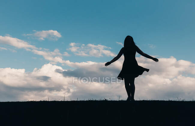 Силует жінки в сукні, що танцює на блакитному небі з хмарами . — стокове фото
