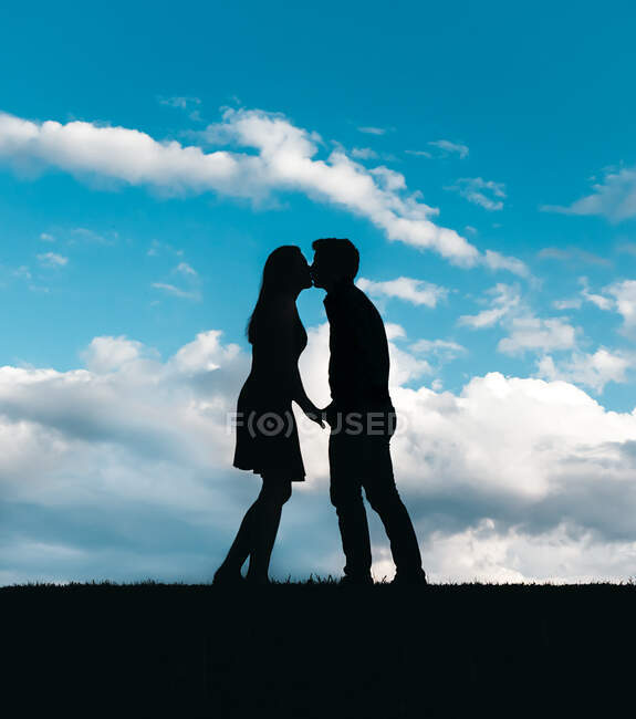 Silhouette di uomo e donna che si baciano contro un cielo blu con nuvole. — Foto stock