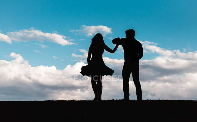 Silhouette of man and woman dancing against a blue sky with clouds. — Stock Photo