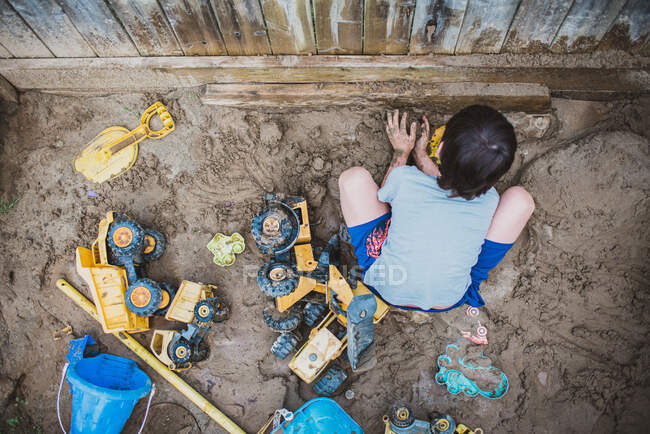 Young boy playing in muddy sandbox in backyard filled with toys. — Stock Photo