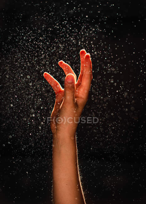 Hand up with water drops on dark background — Stock Photo