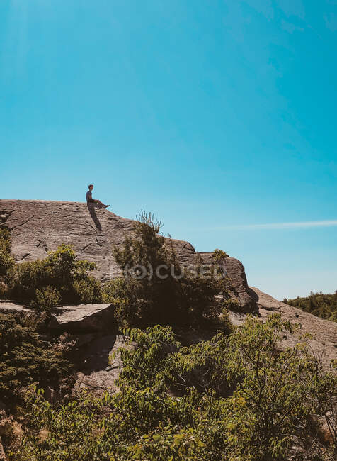 Teen boy sitting on top of a rocky hill on a hike on a sunny day. — Stock Photo