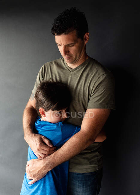 Retrato de un niño abrazando a su padre contra un fondo negro. - foto de stock