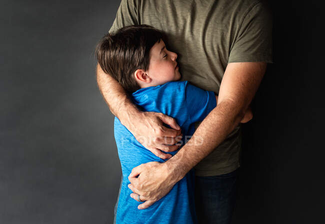 Nahaufnahme eines kleinen Jungen, der seinen Vater vor schwarzem Hintergrund umarmt. — Stockfoto