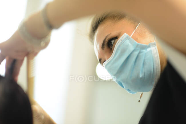 Femme coiffeuse au travail portant un masque facial tout en coiffant jeune gir — Photo de stock