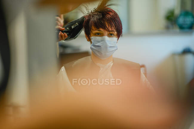 Female hair stylist at work wearing face mask while styling woman — Stock Photo