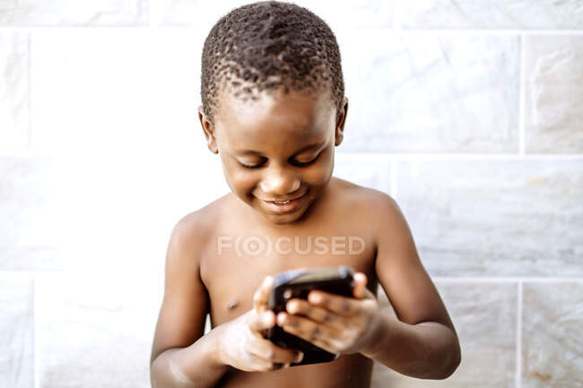 Buen chico africano se divierte usando un teléfono móvil. - foto de stock