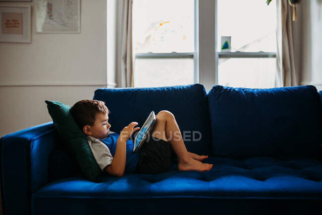 Mignon petit garçon en utilisant tablette sur canapé — Photo de stock