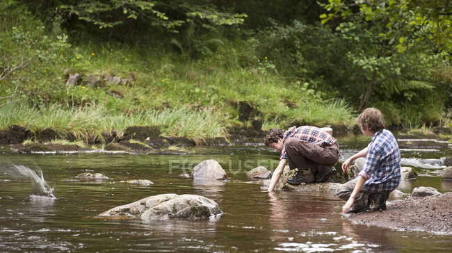 Two brothers skipping stones at small river in the Brecon Beacons — Stock Photo
