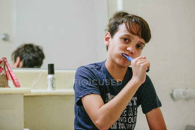 Garçon se brosse les dents dans la salle de bain tout en regardant la caméra — Photo de stock