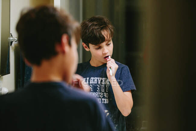 Reflet d'un garçon dans un miroir de salle de bain en soie dentaire — Photo de stock