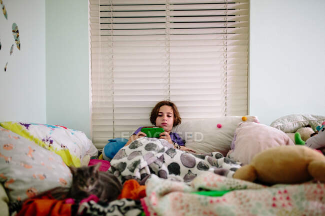 Menina adolescente deitada na cama com seu gato e seu jogo de vídeo portátil — Fotografia de Stock