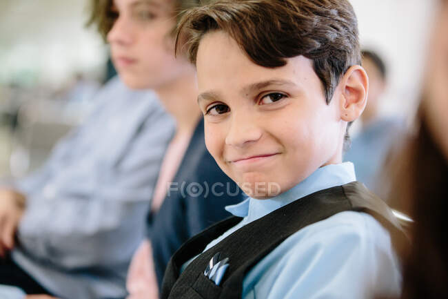 Niño sentado y vestido con chaleco y botón sonríe a la cámara - foto de stock