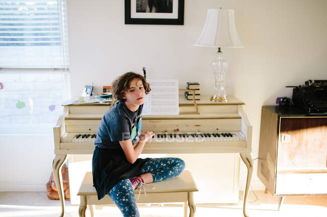 Chica adolescente sentada en el banco de piano toca las teclas de piano detrás de ella - foto de stock
