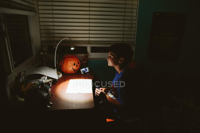 Хлопчик сидить у темряві за своїм столом під час відеодзвінка з другом. — стокове фото