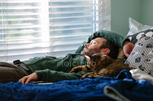 Mann macht ein Katzenschläfchen mit seiner gestromten Katze, die neben ihm kuschelt — Stockfoto