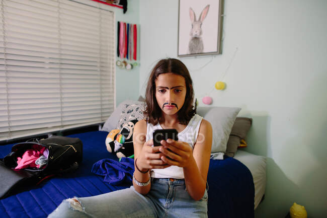 Tween girl takes a serious selfie while wearing a painted on mustache — Stock Photo
