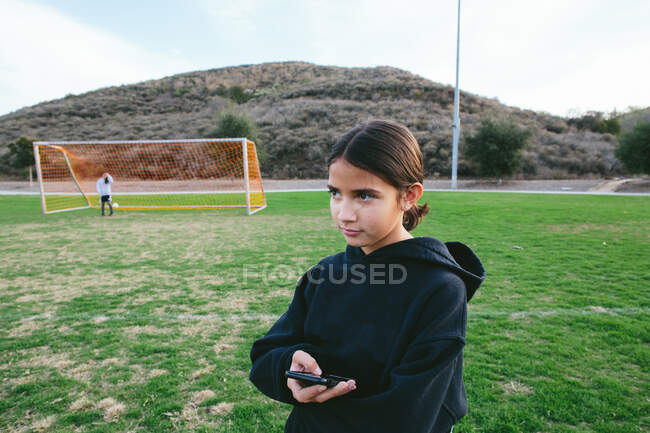 Tween chica sostiene su teléfono celular mientras mira apagado mientras que en un parque - foto de stock