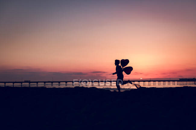 Silhouette eines Jungen mit Luftballons am Strand — Stockfoto
