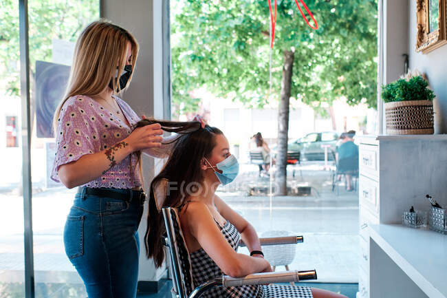 A hairdresser wearking a face mask making curls at the beatuy saloon - coronavirus crisis concept — Stock Photo