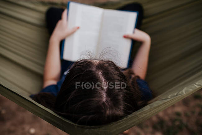 Центральная верхняя рама девочки-подростка, читающей в гамаке — стоковое фото